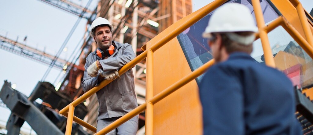 Two men in hard hats talking in chemical and petrochemical work environment