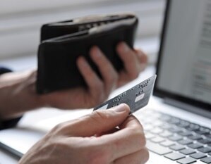 Person with wallet and credit card in hand near laptop