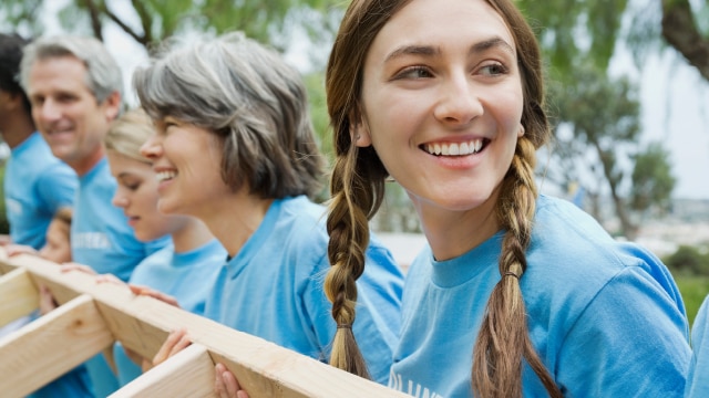 Volunteers smiling and holding up a wooden houseframe