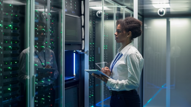 Woman standing in server room and looking at pieces of technology
