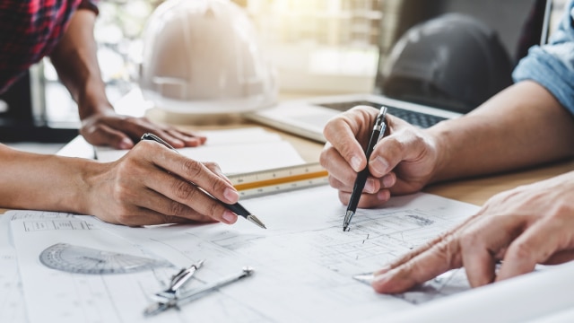 Two people looking at blueprints on a drafting table