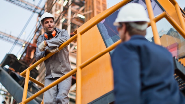 Two men wearing hardhats on a production site having a conversation