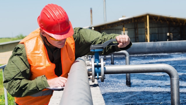 Man in hardhat and high visibility vest fixing a pipe with a wrench