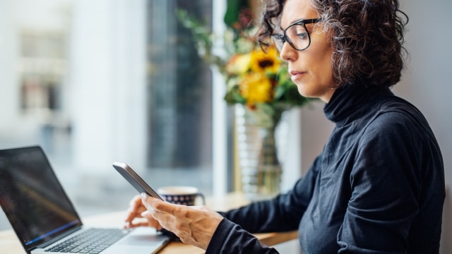 Woman sitting at her desk and looking at her phone and laptop