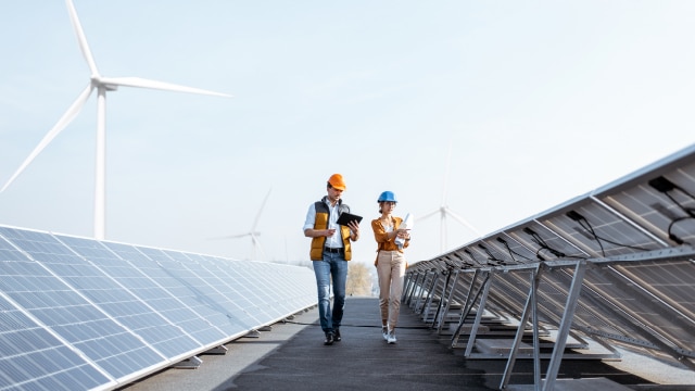 Man and woman walking through an area filled with solar panels and win turbines