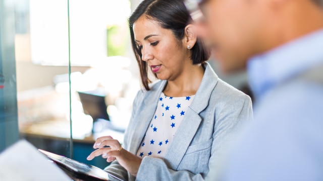 Woman looking at electronic tablet while sitting next to her colleague