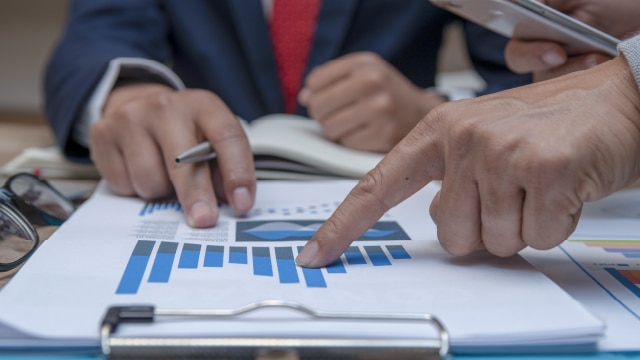 Two sets of hands pointing at graphs on a clipboard