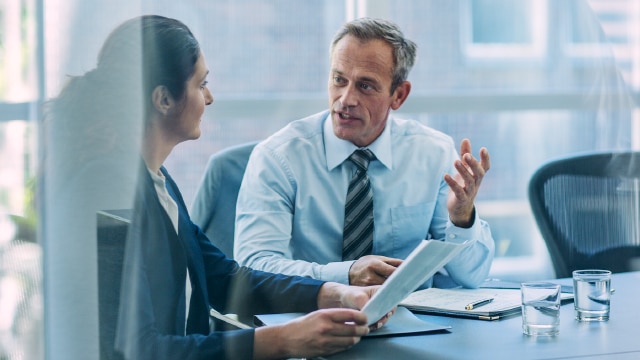 Two business people having a discussion in a glass office while sitting down